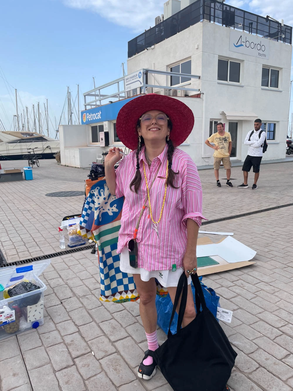 Mujer con un sombrero rojo de ala ancha sonriendo en un puerto deportivo durante un rodaje de Glassy Films