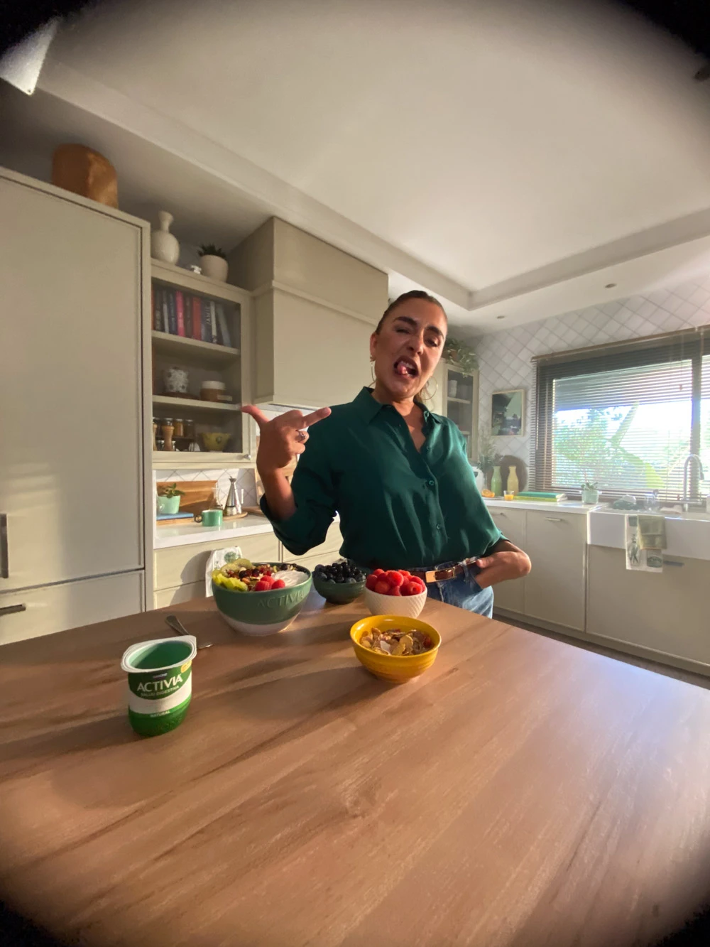 Actress joking in a kitchen behind an Activia yogurt and fruit bowls, on set